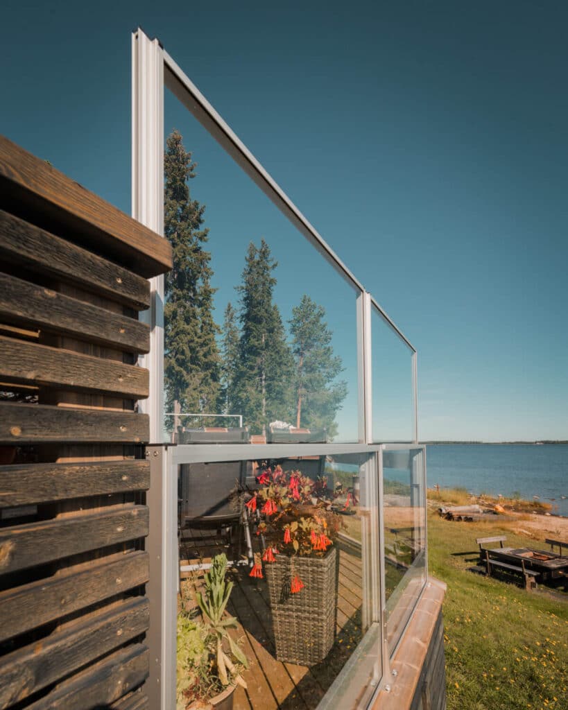 Rambarde en verre réglable montée sur terrasse au bord de l’eau, protégeant du vent sans masquer la vue.