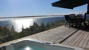 Terrasse en bois avec garde-corps en verre sans poteaux, meubles d’extérieur et vue dégagée sur la mer.