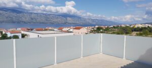 Balcon avec garde-corps en verre dépoli et poteaux en aluminium blancs – vue sur mer, montagnes et toits.