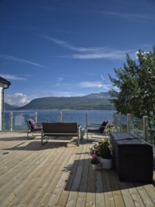 Grande terrasse avec garde-corps en verre et poteaux bois – vue panoramique sur le lac et ambiance lounge élégante.