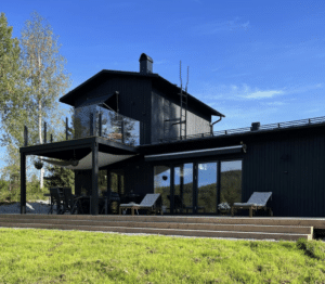 Garde-corps moderne en verre fumé avec poteaux noirs, monté sur terrasse haute avec façade bois foncé.