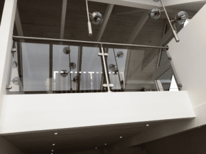 Garde-corps en verre teinté monté sur une mezzanine moderne avec éléments en acier inoxydable et plafond à poutres apparentes.