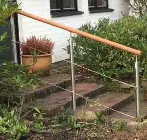 Rampe extérieure avec main courante en bois et câbles inox, installée le long d'un escalier de jardin en briques.