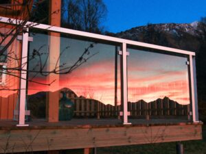Balustrade en verre avec montants blancs reflétant un coucher de soleil coloré sur fond de montagnes.
